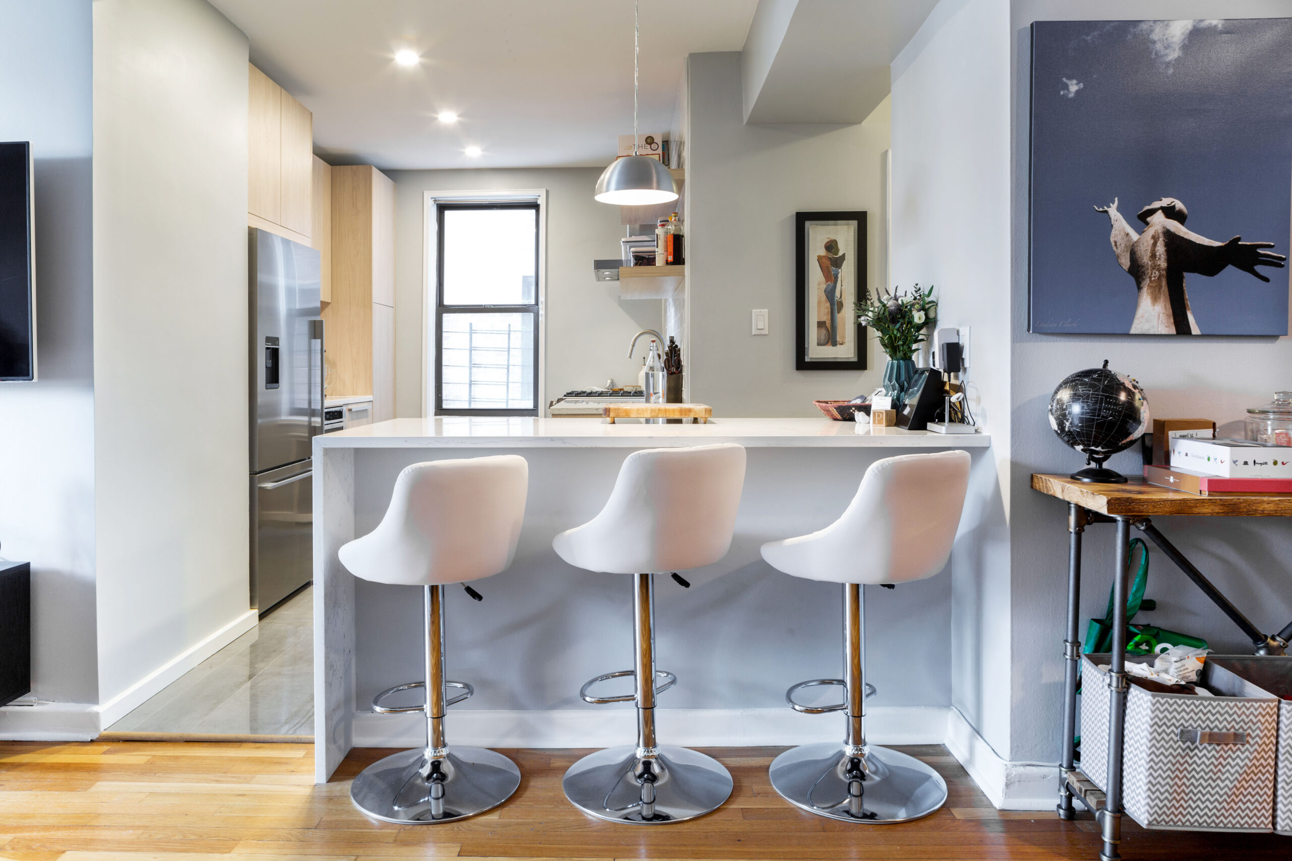 Open plan kitchen living room in Ditmas Park with a three-seat peninsula, light wood cabinets, white counters, and a clear view into the kitchen.