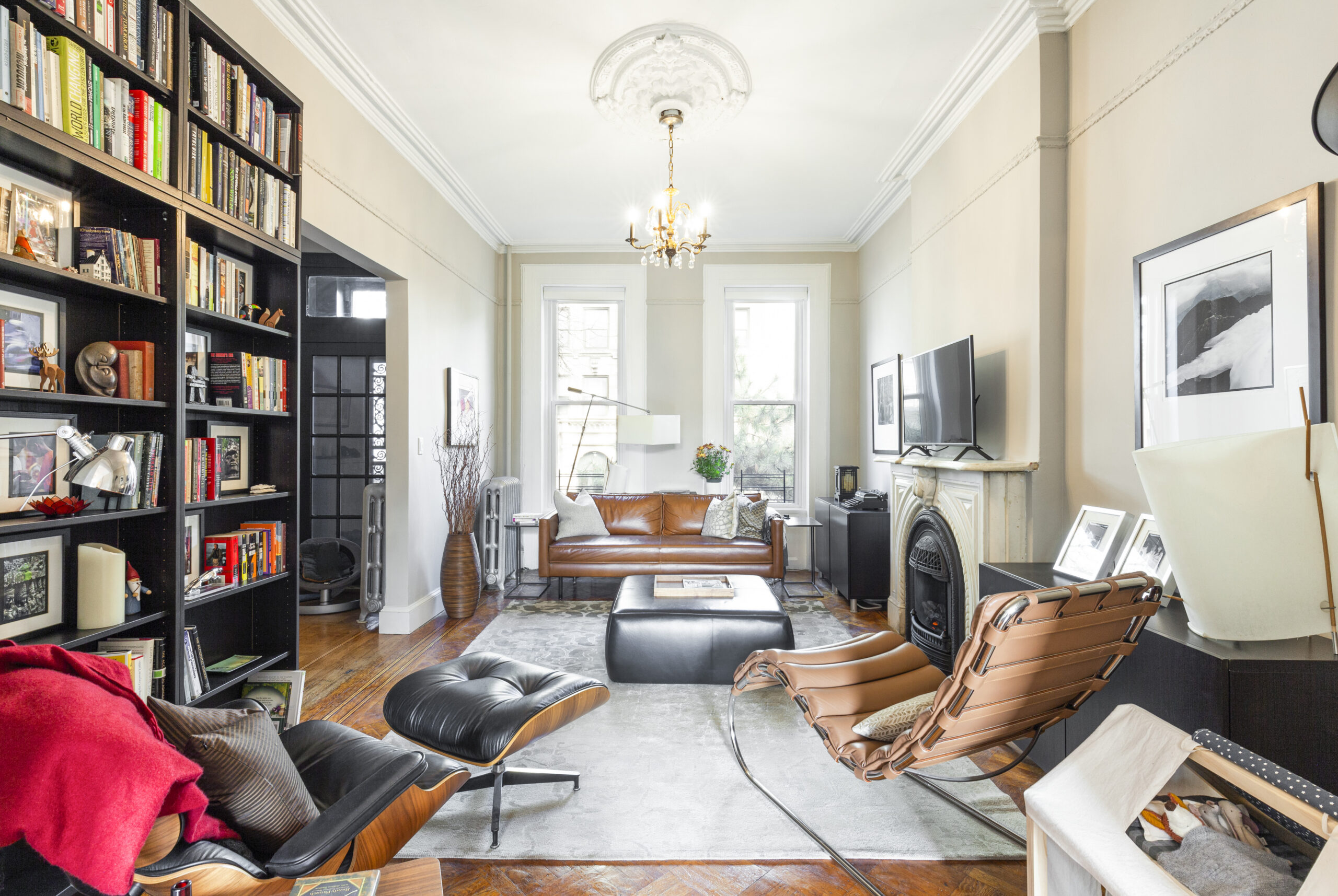 Park Slope townhouse living room with restored wood floors, original fireplace, tall windows, built-in bookshelves, crown molding, and mixed modern seating.