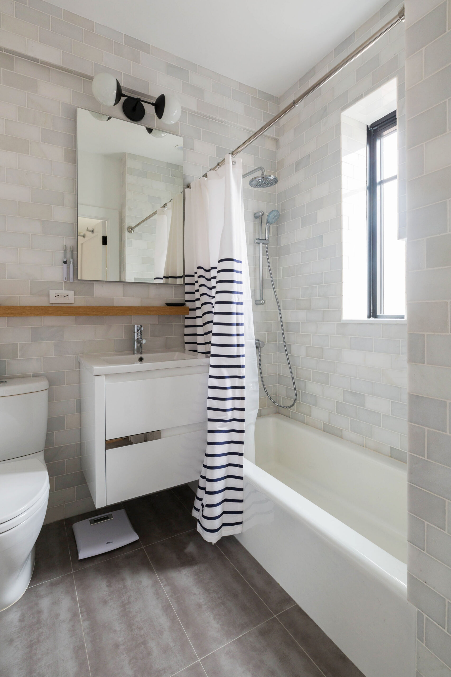 Pale subway tile wraps a tub-shower beside a tall existing window, integrating the bathing area with natural light in this Prospect Heights bathroom.