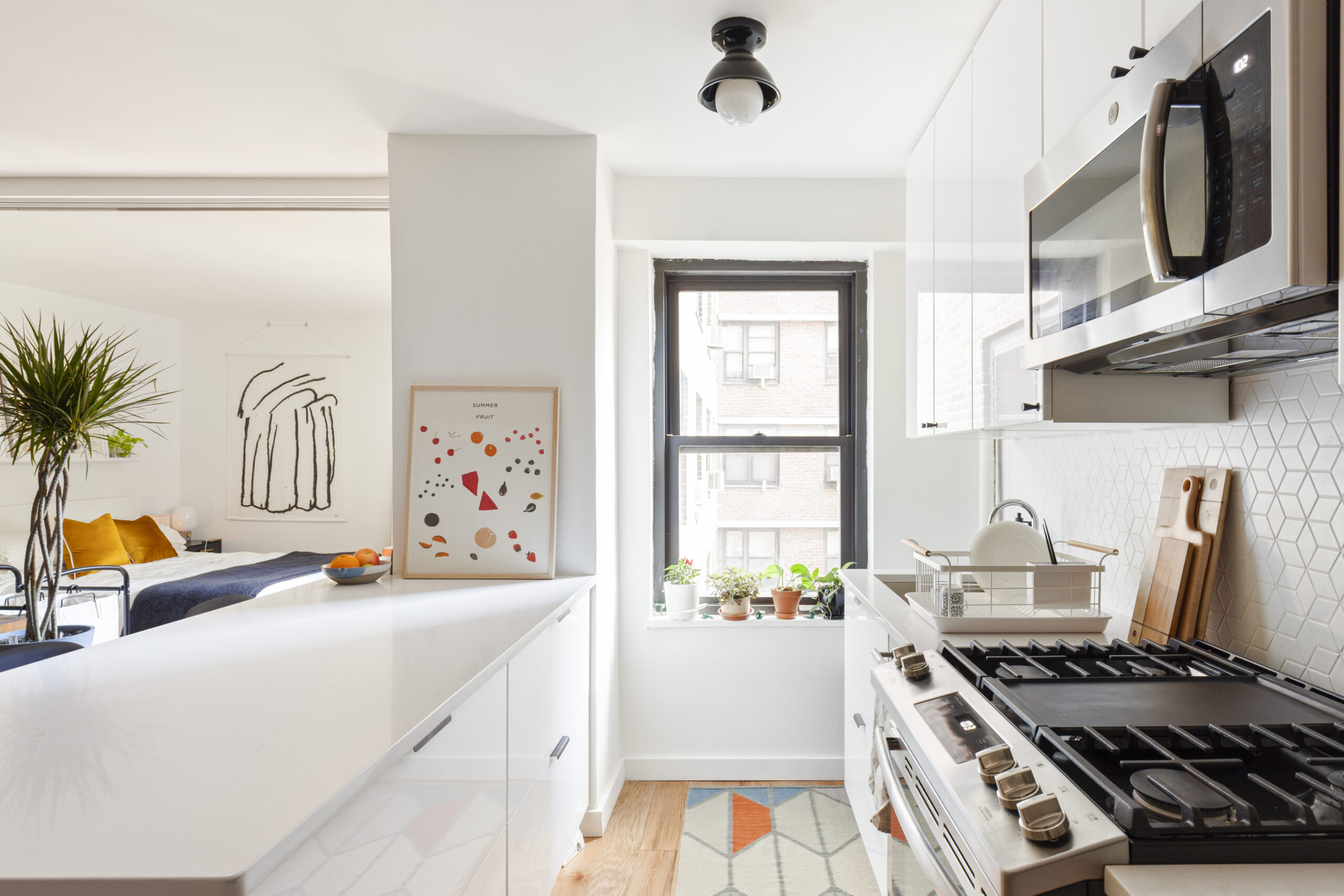 Lower East Side studio apartment with a white kitchen peninsula, geometric tile backsplash, stainless steel range, and sleeping area visible beyond.
